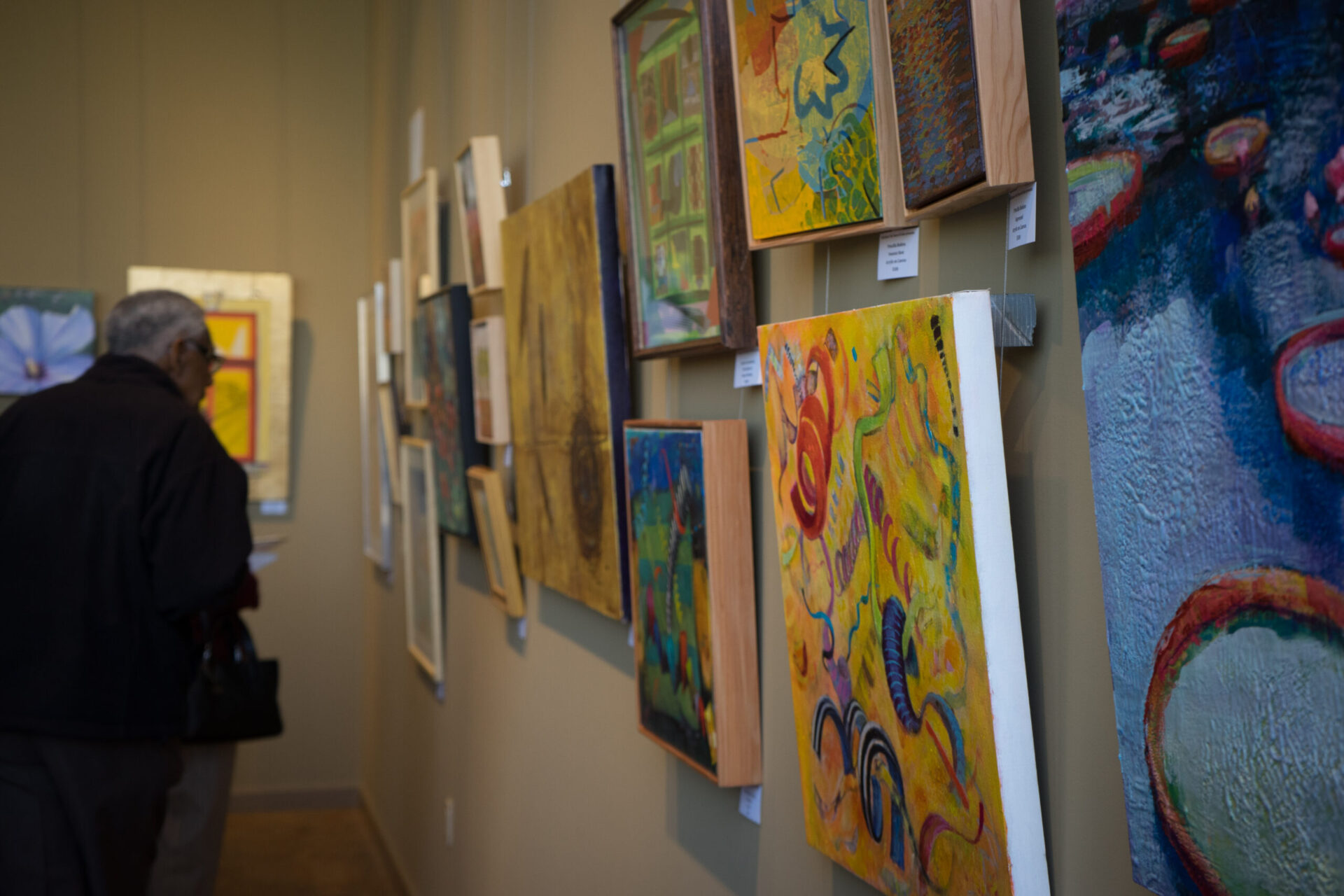 A man looks at paintings hanging on the wall at Jenkins with a bright yellow piece in the foreground.